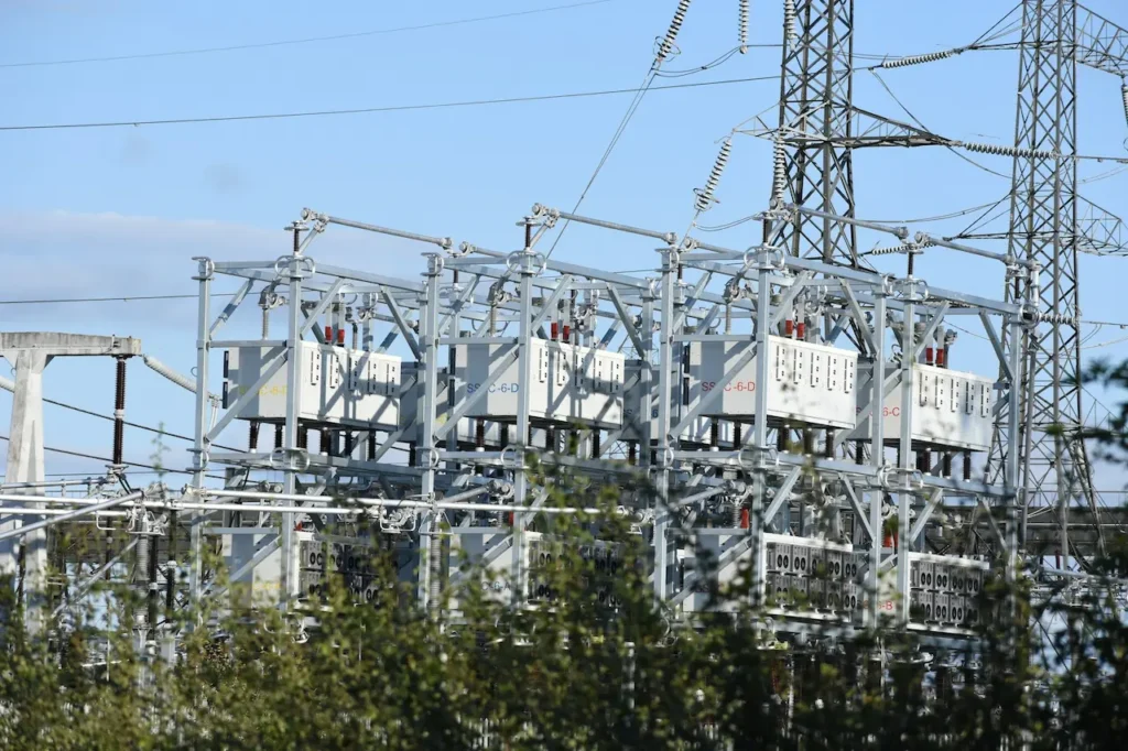High-Voltage Power Substation A detailed view of an electrical substation, featuring a complex network of high-voltage transformers, switchgear, and insulators on a steel lattice structure under a bright blue sky.